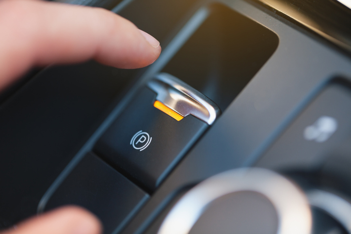 Close-up of a finger pressing a vehicle parking brake button, representing safety-critical interior controls protected by flame retardant materials